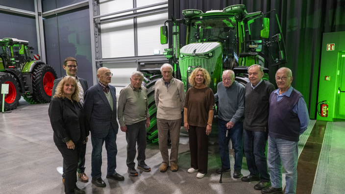 A group of people standing in front of a green tractor in a showroom.