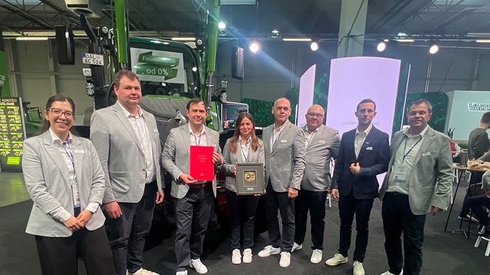 A group of people standing in front of a tractor displaying an award in an exhibition hall.