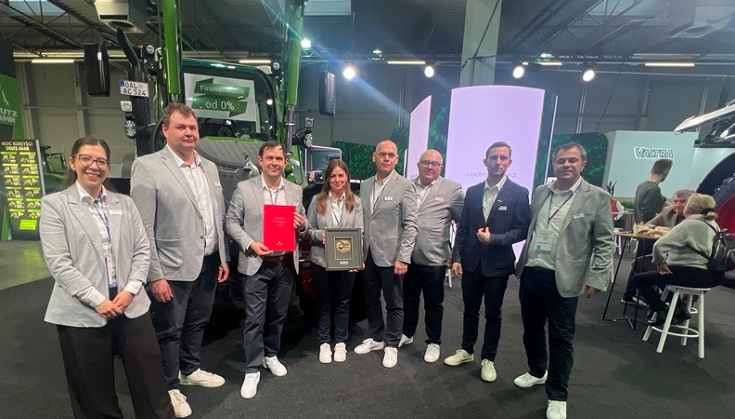 Expert jury honours the new generation of the Fendt 500 Vario in Poland A group of people standing in front of a tractor displaying an award in an exhibition hall.