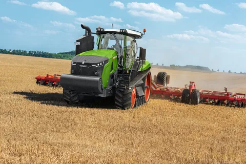 Vista laterale di un Fendt 1100 MT Vario al lavoro in un campo con un attrezzo verde su un campo di stoppie. Sullo sfondo si vede un cielo azzurro con alcune nuvole sparse.