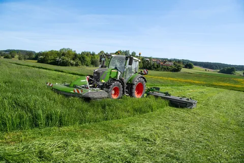 un Fendt 300 Vario verde falcia con una falciatrice anteriore e posteriore Fendt Slicer su un prato scosceso.