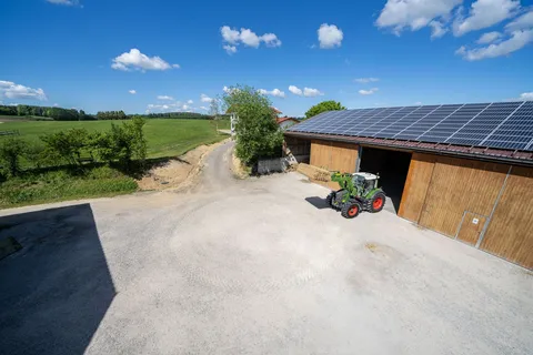 Un Fendt 500 Vario verde esce da un capannone con il caricatore frontale sollevato e una balla.