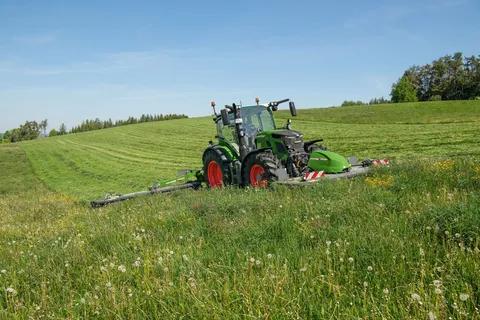 Un Fendt 500 Vario verde falcia un prato con una falciatrice anteriore e una posteriore.