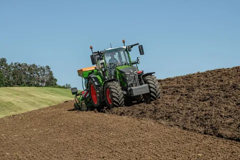 Un Fendt 500 Vario verde con una combinazione di seminatrici Amazone verde-arancione semina su un campo.