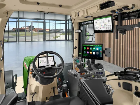 Una foto dell'interno della cabina del trattore dal punto di vista del conducente con volante, bracciolo di comando FendtONE con joystick e Apple CarPlay sul terminale, nonché un terminale aggiuntivo sul tetto.