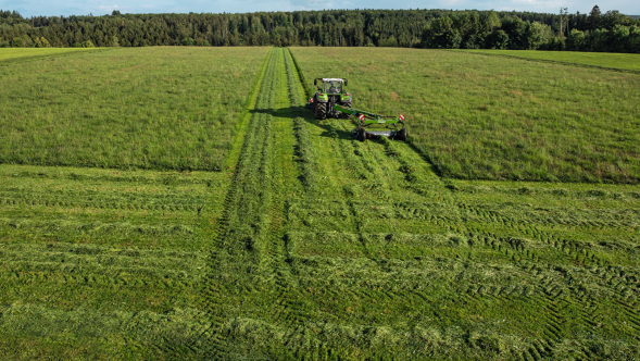 Fendt Slicer trainata con carrello di trasporto in una prateria Fendt Slicer trainata con carrello di trasporto e falciatrice frontale su una prateria. Sullo sfondo è visibile un bosco.