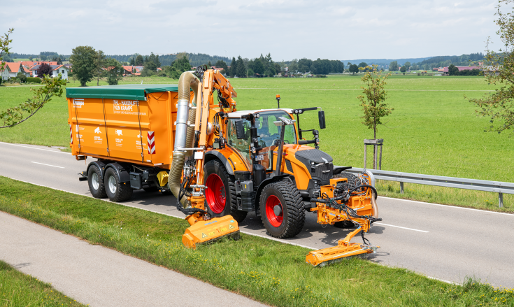 Fendt 728 Vario in arancione municipale con braccio decespugliatore durante i lavori di sfalcio Fendt 728 Vario in arancione municipale con due bracci decespugliatori per lavori di falciatura stradale e con rimorchio