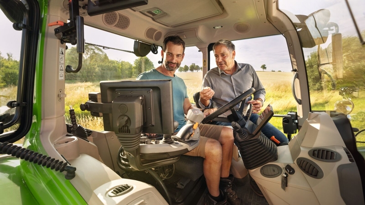 Un agricoltore e un concessionario Fendt sono seduti nella cabina di un trattore Fendt e guardano il terminale.