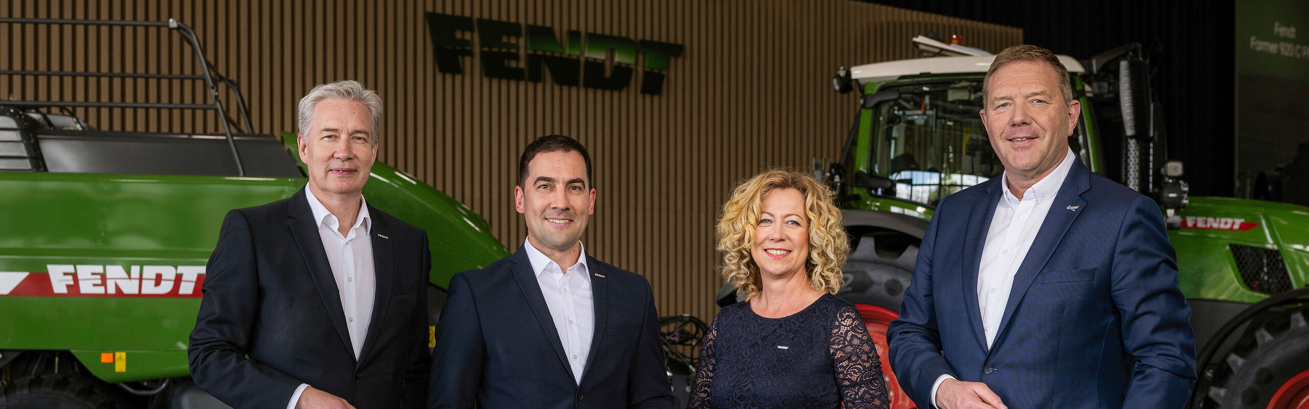 Da sinistra a destra, gli amministratori delegati Ekkehart Gläser, Dr Josef Mayer, Ingrid Bußjäger-Martin e Christoph Gröblinghoff si trovano uno accanto all'altro nel Forum Fendt davanti a un trattore Fendt e alla pressa quadra Fendt.