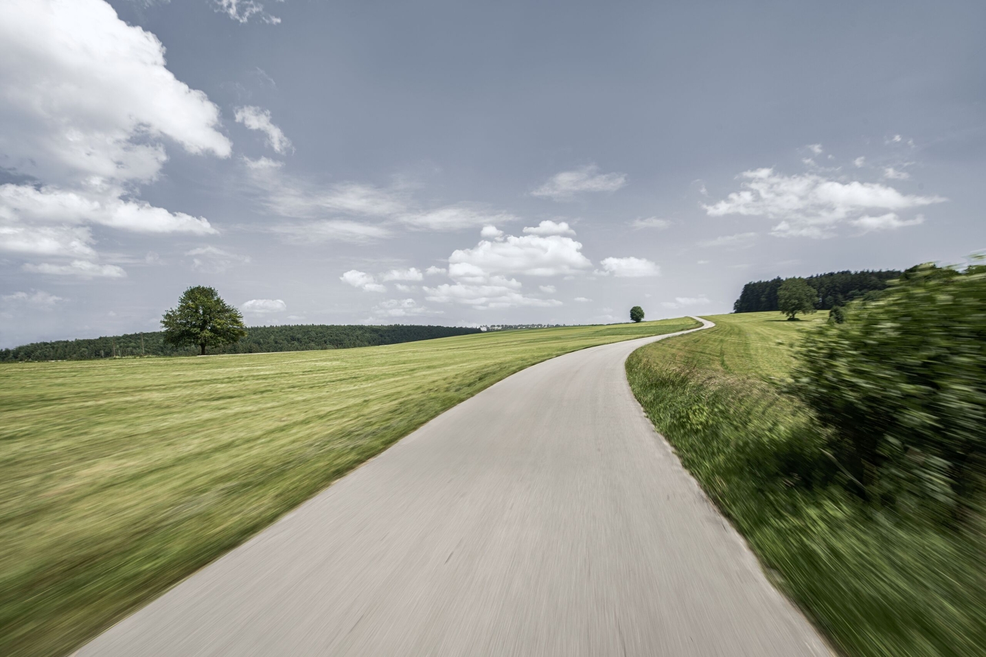 Una strada di campagna conduce, con delle curve, attraverso campi verdi