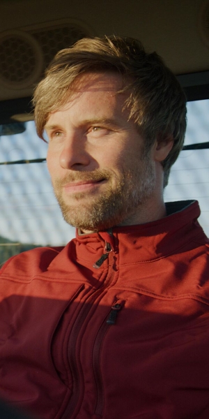 Un giovane agricoltore con gilet rosso procede sorridente all’interno della cabina della sua macchina Fendt