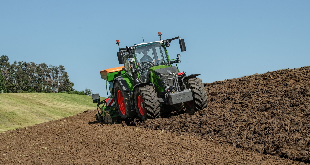 Un Fendt 500 Vario verde con una combinazione di seminatrici Amazone verde-arancione semina su un campo.