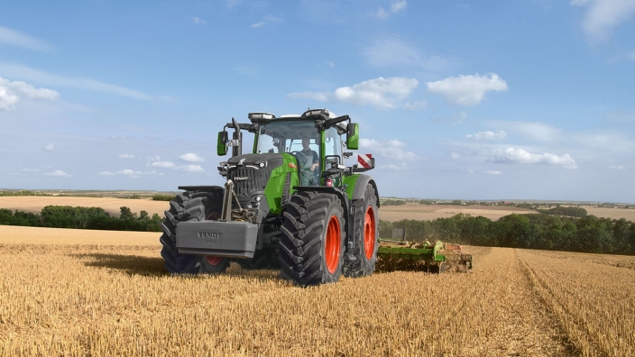 un Fendt 800 Vario lavora con un erpice di Amazone su un campo di stoppie verde-arancione.