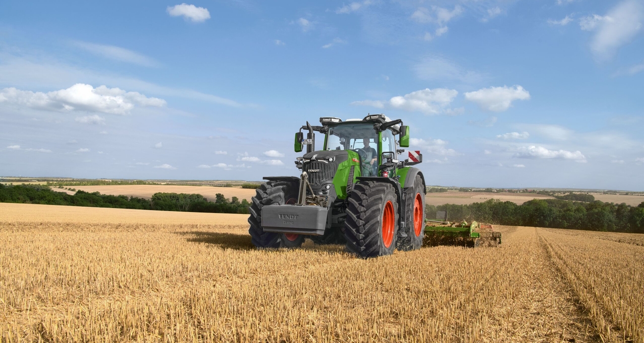 un Fendt 800 Vario lavora con un erpice di Amazone su un campo di stoppie verde-arancione.