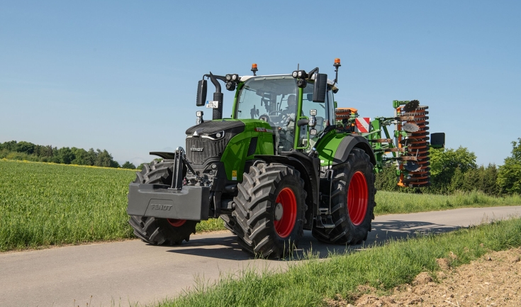 un Fendt 724 Vario Gen7.1 verde trasporta un coltivatore Amazone in posizione di trasporto su una strada.