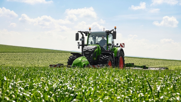 Un Fendt 600 Vario con attrezzo montato che lavora in un campo verde sotto un cielo blu