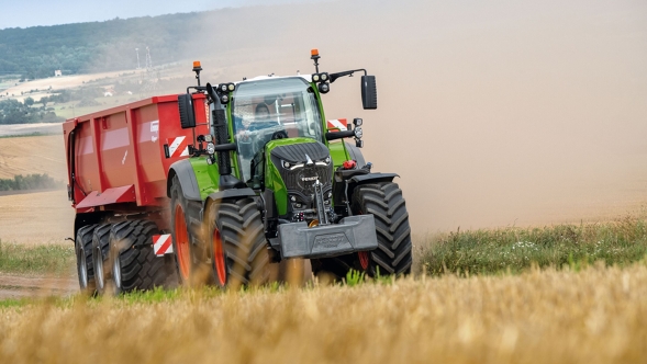 Un agricoltore guida un Fendt 700 Vario Gen7 e un cassone ribaltabile rosso su un campo.