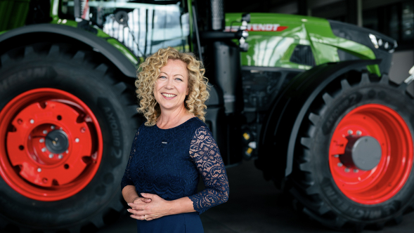 Ingrid Bußjäger-Martin está em um vestido azul escuro em frente a um trator Fendt Priešais „Fendt“ traktorių stovi tamsiai mėlyną suknelę vilkinti Ingrida Busjėger-Martin (Ingrid Bußjäger-Martin)