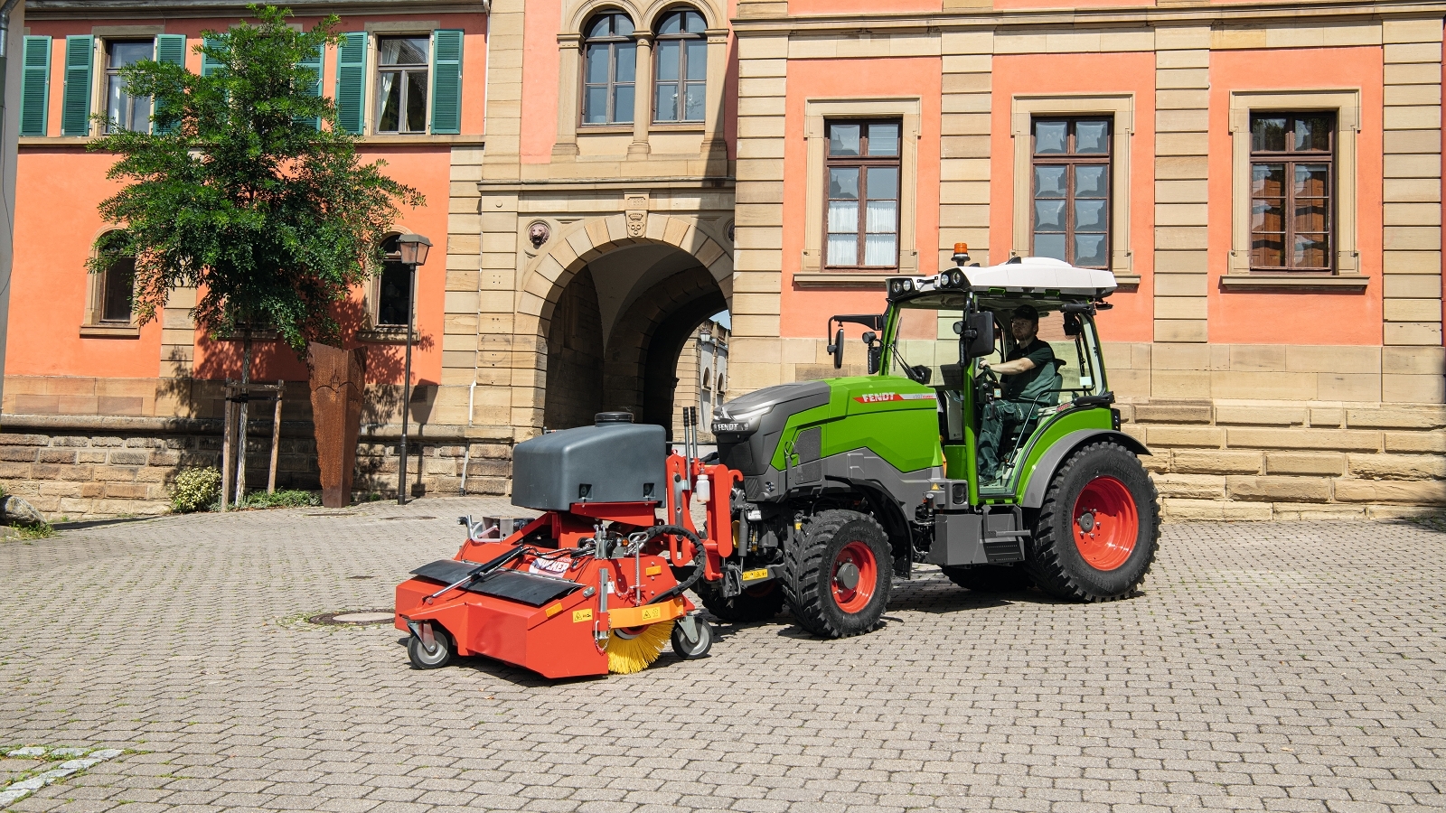 Komunalinėms reikmėms naudojamas „Fendt e100 V Vario“ Priešais visuomeninį pastatą stovi „Fendt e100 V Vario“