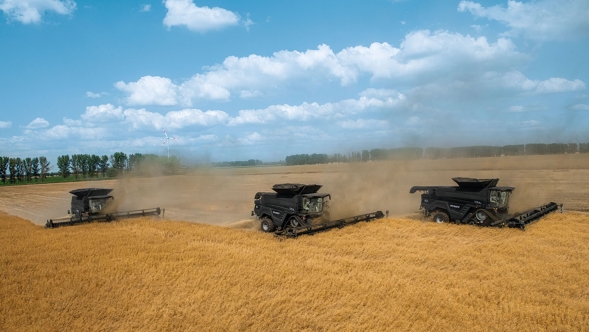 Trys „Fendt IDEAL“ Kviečių lauke dirba trys „Fendt IDEAL“. Fone matosi medžiai ir mėlynas, šiek tiek debesuotas dangus.