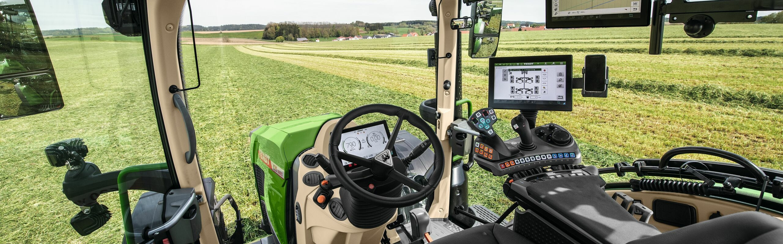 „Fendt 600 Vario“ kabinos salono vaizdas su vaizdu į žalią pievą.