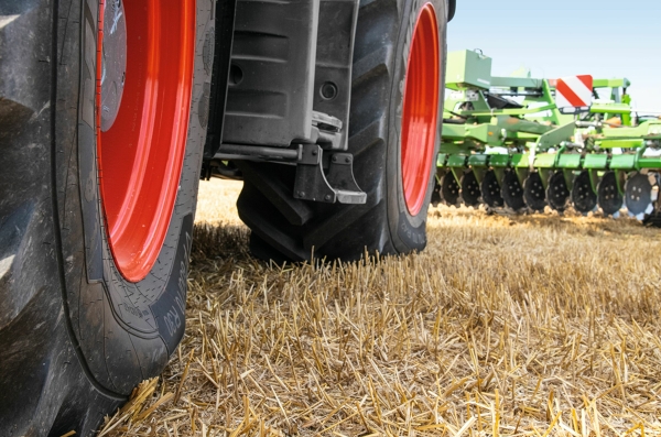 Traktoriaus padangos Dviejų juodų traktoriaus padangų raudonais ratlankiais, stovinčių šviesiai rudame lauke, vaizdas iš arti. Fone matosi žalias „Fendt“ padargas.