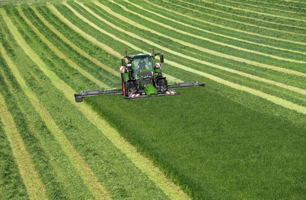 Žalioje pievoje žaliu padargu „Fendt Slicer“ šienauja žaliasis traktorius „Fendt 600 Vario“, fone matyti šienavimo pėdsakai.