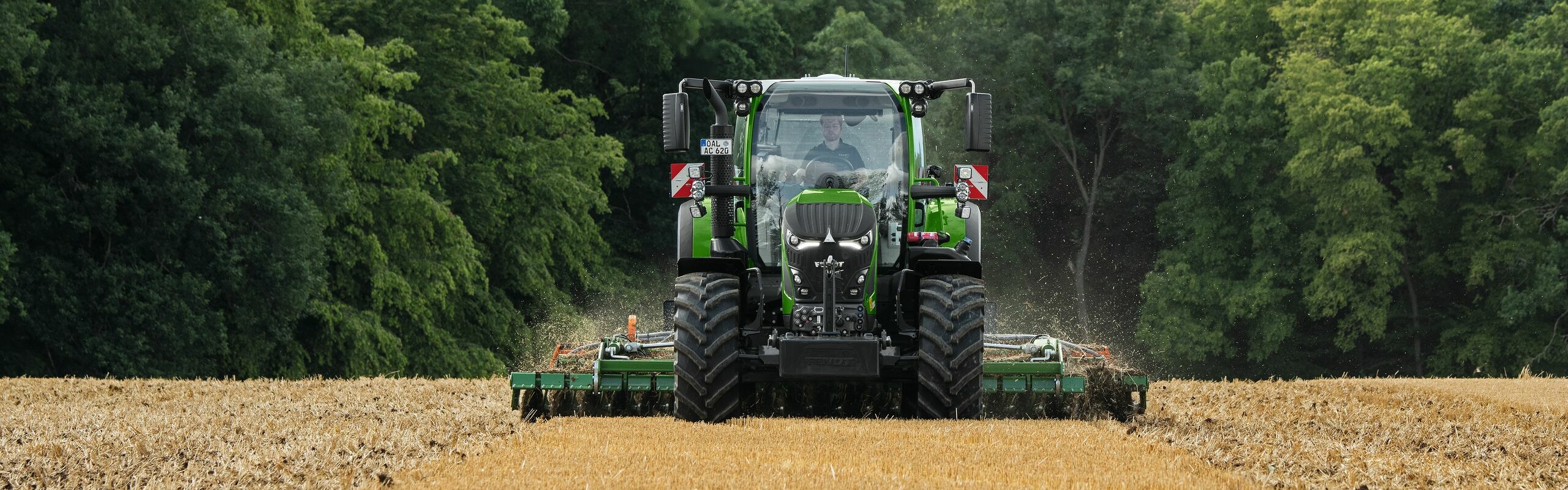 Rudame lauke su padargu dirbantis žaliasis „Fendt 600 Vario“. Fone tamsiai žaliai miškas ir debesuotas dangus.