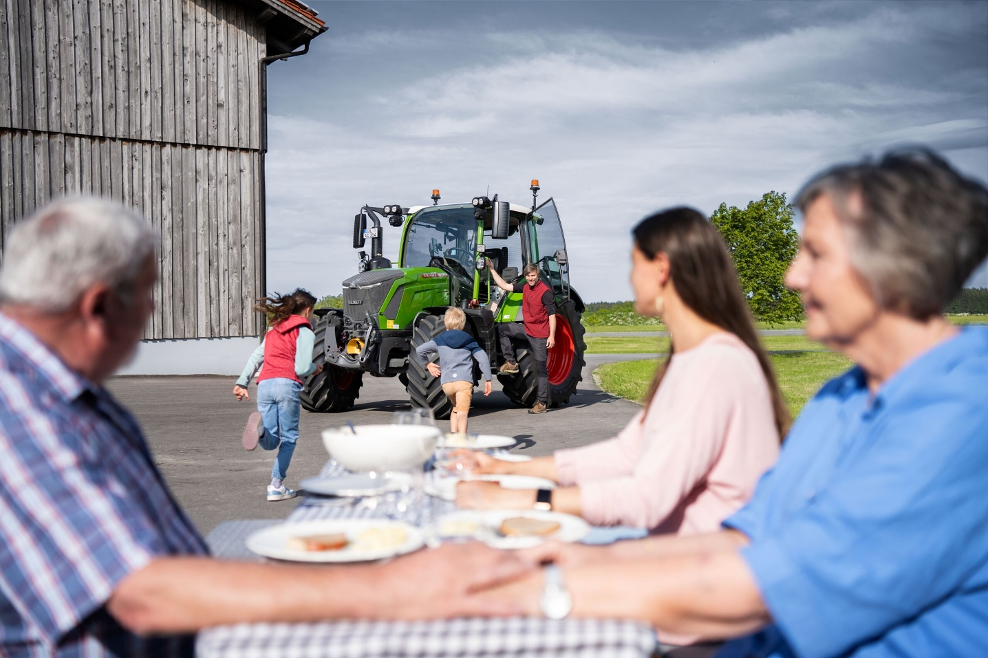 Savo ūkyje prie padengto stalo sėdi šeima ir džiaugiasi paskutinių dviejų šeimos narių atvykimu: ūkininku ir „Fendt 300 Vario“