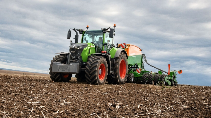 Lauke su sėjamąja dirbantis „Fendt 700 Vario“. Fone matosi debesuotas dangus.