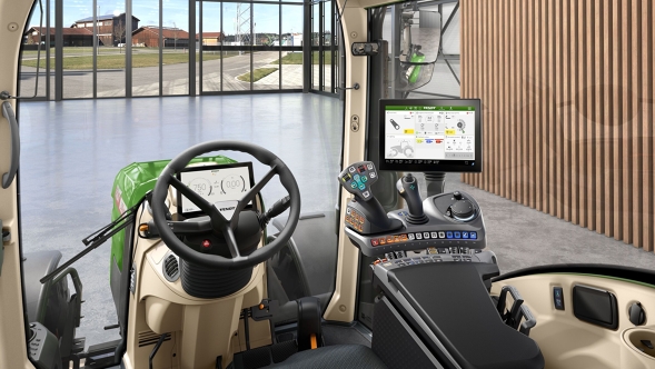 „Fendt 300 Vario Gen5“ „VisioPlus“ kabinos su ergonomiška valdymo svirtimi, vairu ir dideliu terminalu vaizdas priešais modernų kiemo foną su stikliniu priekiu.