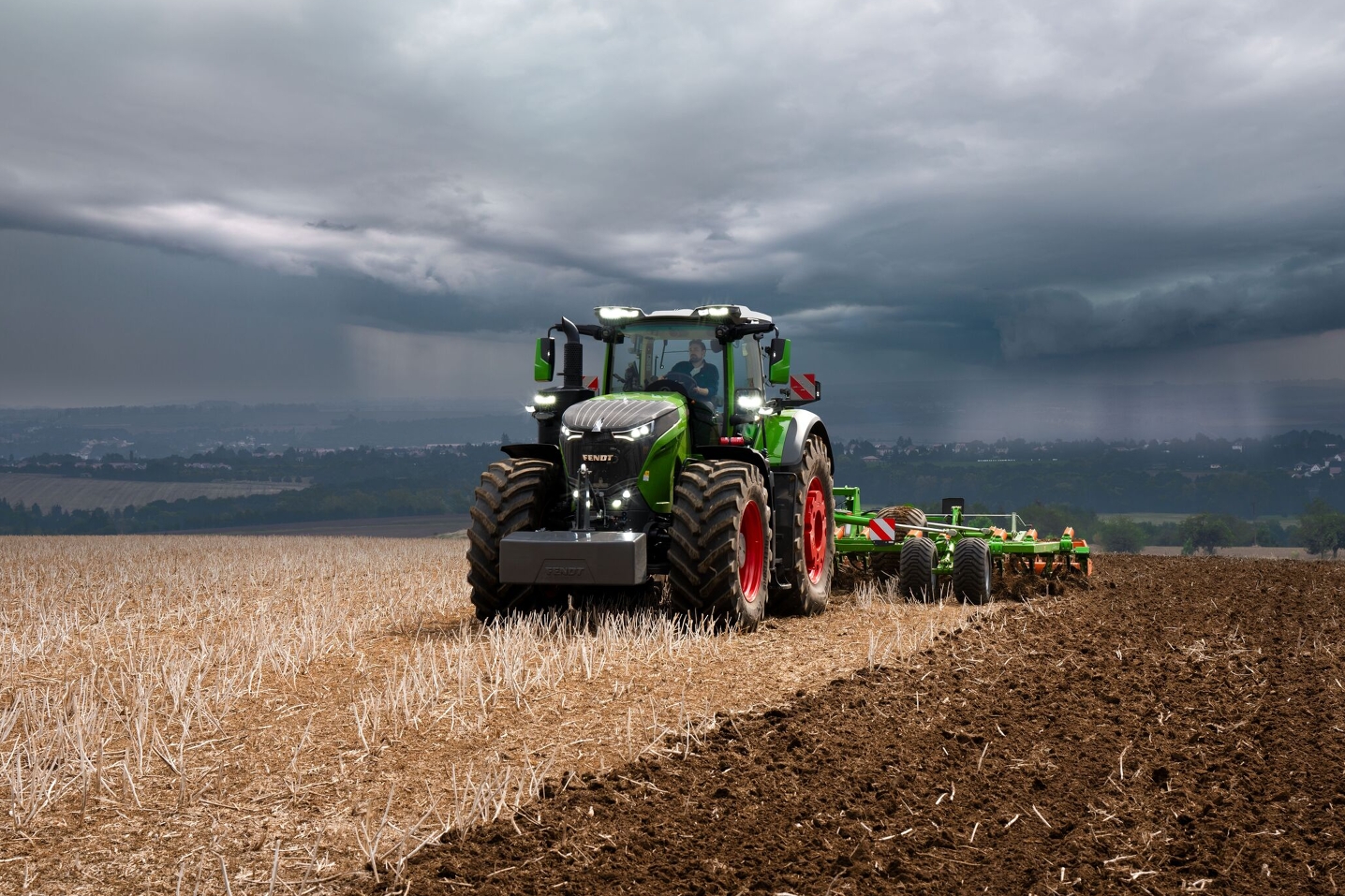 Priešais sunkius, besidriekiančius audros debesis tolumoje „Fendt 1000 Vario“ traktorius galingai dirba lauko darbus