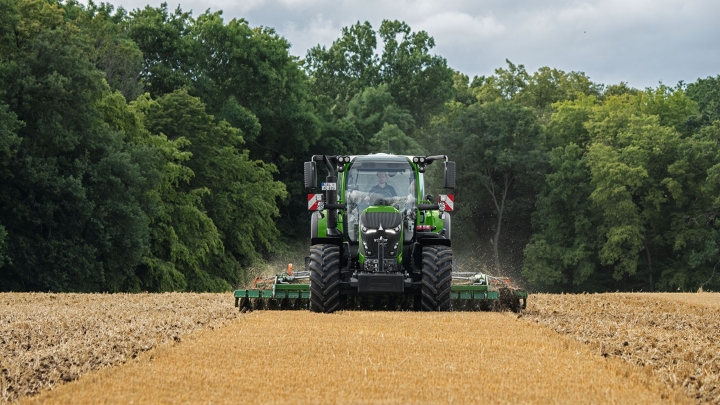 Rudame lauke su padargu dirbantis žaliasis „Fendt 600 Vario“. Fone tamsiai žaliai miškas ir debesuotas dangus.
