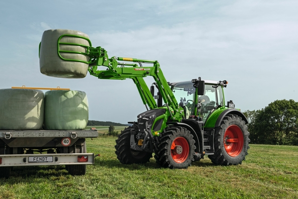 Fendt 600 Vario ar Fendt Cargo frontālo iekrāvēju Zaļais Fendt 600 Vario traktors ar sarkaniem atlokiem un zaļais Fendt Cargo frontālais iekrāvējs iekrauj apaļās ķīpas iekraušanas laukumā.