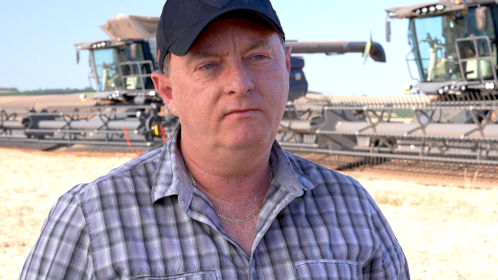 Portrets ar lauksaimnieku, kurš valkā rūtainu kreklu un beisbola cepuri, ar divām lielām Fendt IDEAL mašīnām laukā