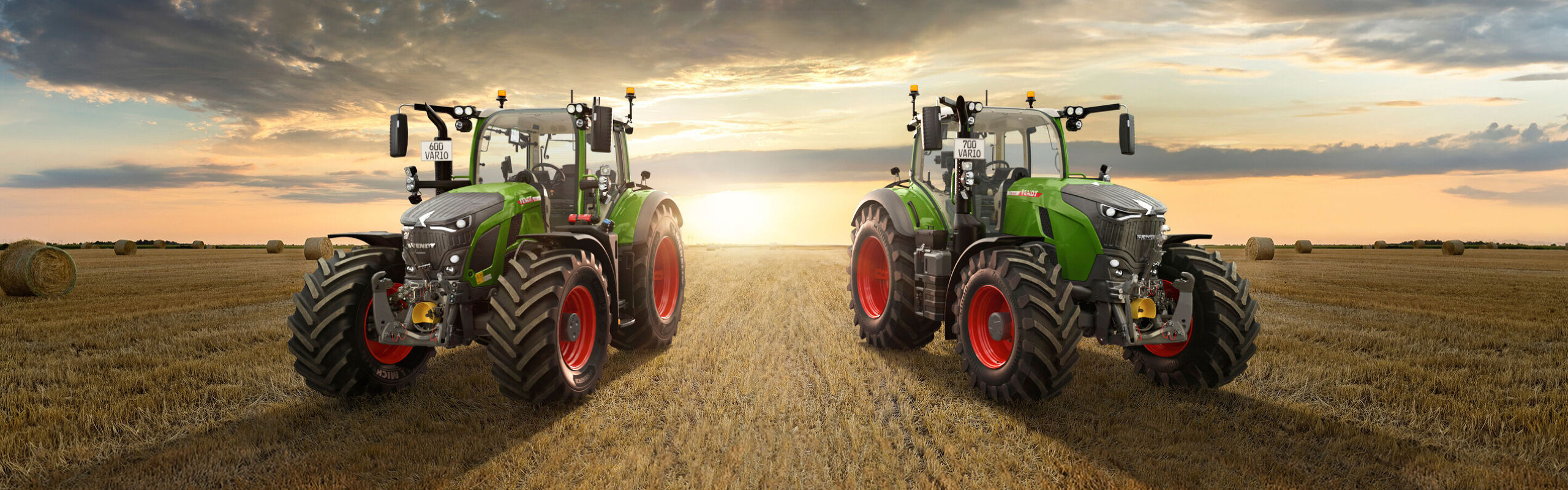 Zaļais traktors Fendt 600 Vario un Fendt 700 Vario Gen7 stāv uz liela lauka ar saulrietu horizontā