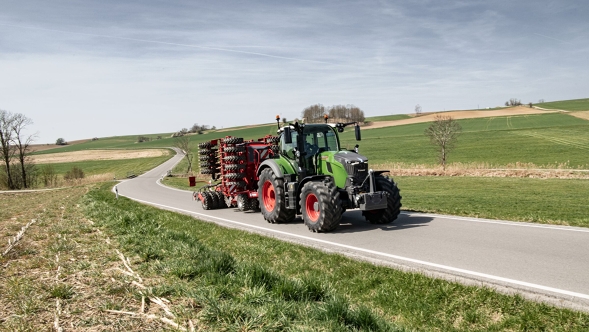 Fendt 700 Vario Gen7.1 ar transporta iekārtu uz ceļa lauku apvidū. Fendt 700 Vario Gen7.1 ar piekabinātu agreāgtu brauc pa lauku ceļu kalnainā pavasara ainavā.