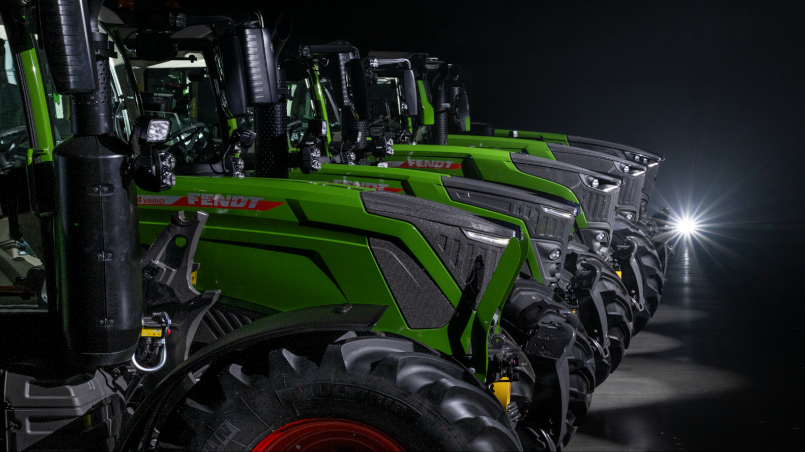 Fendt 300, 500, 700 Vario, 800 un 1000 Vario Jaunie Fendt 300, 500, 700 Vario, 800 un 1000 Vario stāv blakus tumšā zālē.