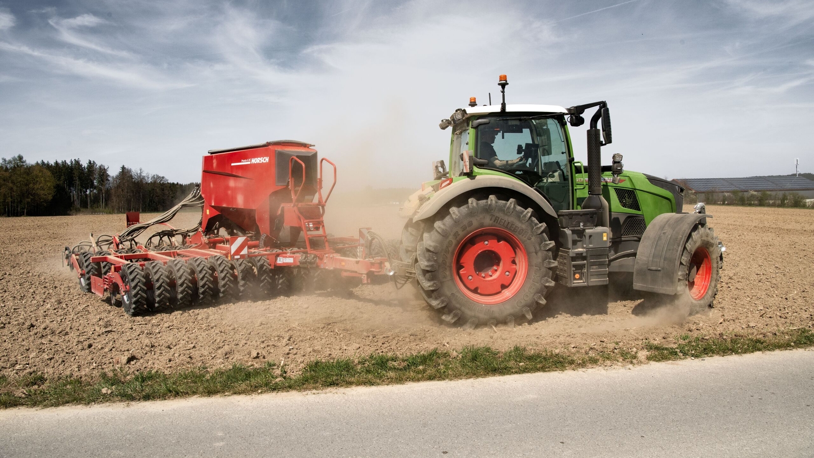 Fendt 700 Vario Gen7.1 ar sarkanu sējmašīnu strādā putekļainā laukā saulainā laikā.