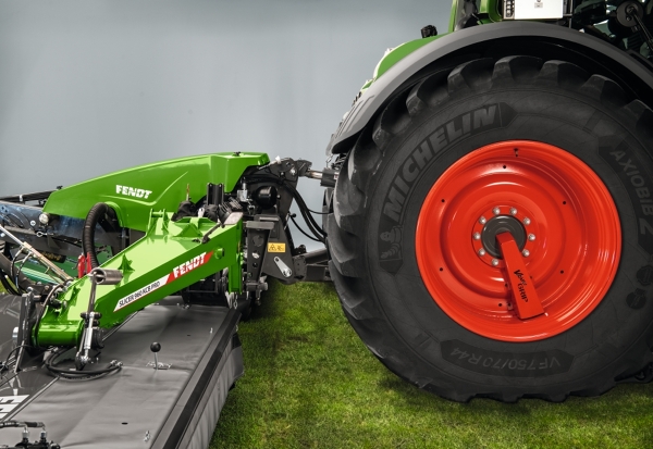 Een Fendt-tractor staat met een Fendt Slicer-schijvenmaaier in de avondschemering op een veld.