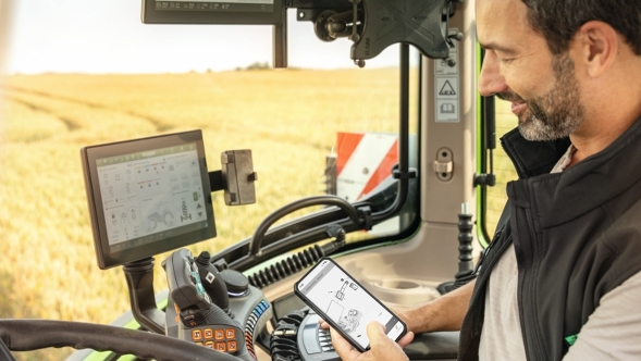 Parts Books to go als app Een boer zit in de trekkercabine en heeft op zijn mobiele telefoon de Parts Books to go-app geopend.