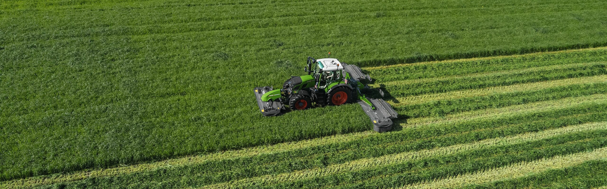 Bovenaanzicht van de groene trekker Fendt 600 Vario met de groene maaier Fendt Slicer op een grote, groene weide.
