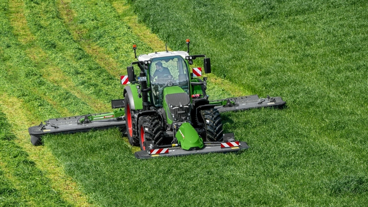 De groene Fendt 600 Vario-trekker maait met de groene aanbouwapparatuur Fendt Slicer op een groene weide. Op de achtergrond zijn maaisporen te zien.