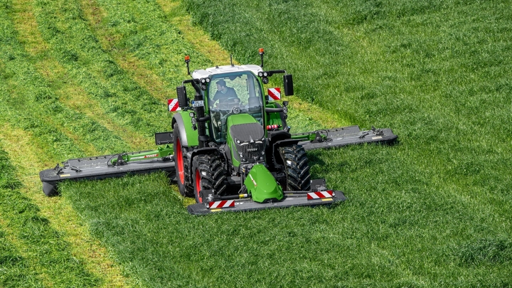De groene Fendt 600 Vario-trekker maait met de groene aanbouwapparatuur Fendt Slicer op een groene weide. Op de achtergrond zijn maaisporen te zien.