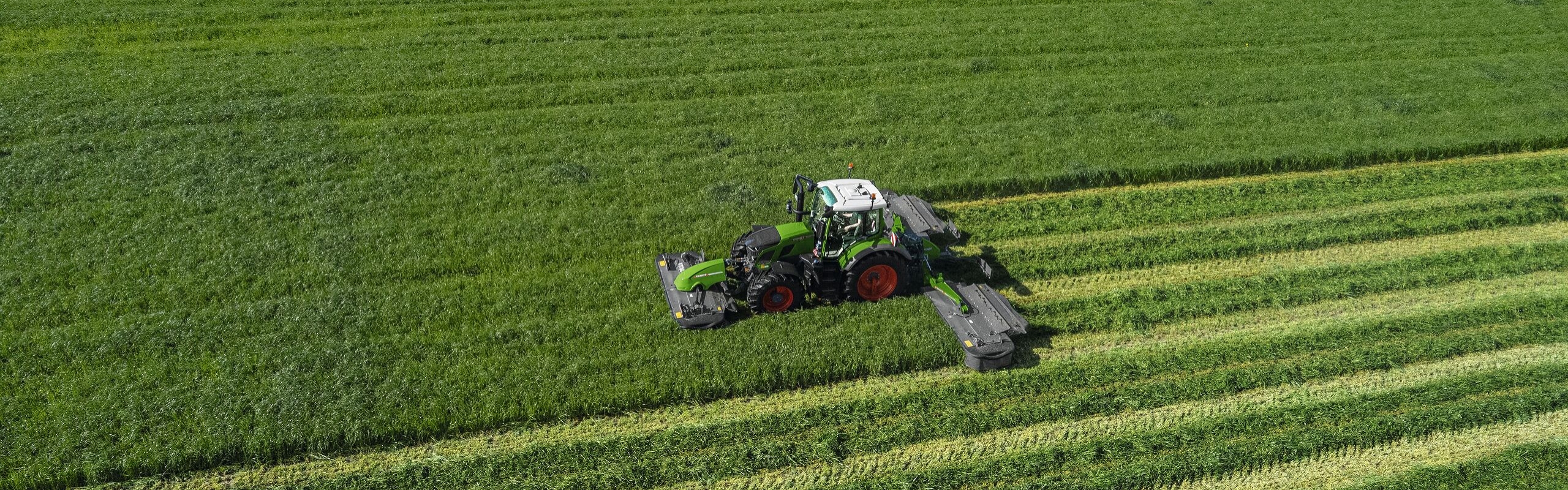 Bovenaanzicht van de groene trekker Fendt 600 Vario met de groene maaier Fendt Slicer op een grote, groene weide.
