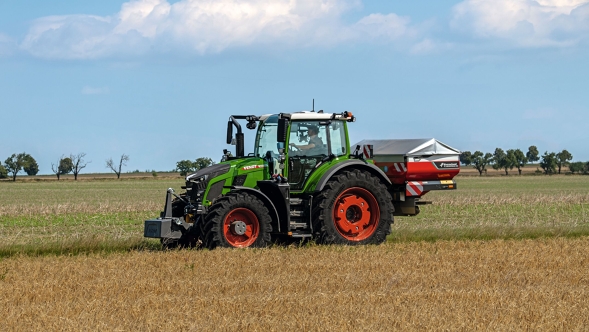 De groene tractor Fendt 600 Vario met rode velgen in een zijaanzicht op een groene weide. Op de achtergrond is een blauwe lucht met witte wolken te zien.