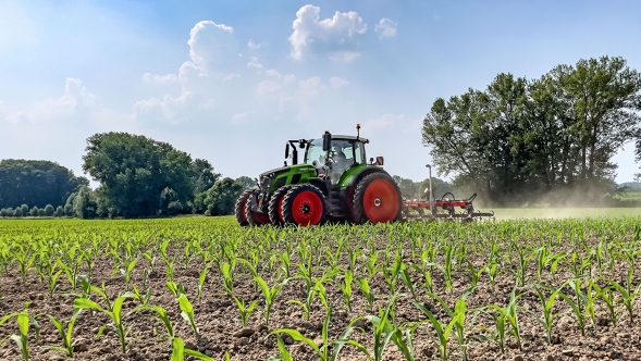 De groene tractor Fendt 600 Vario met dubbele banden aan het werk op akkerbouwgrond. Op de achtergrond zijn donkergroene bomen een een lichtblauwe lucht met witte wolken te zien.