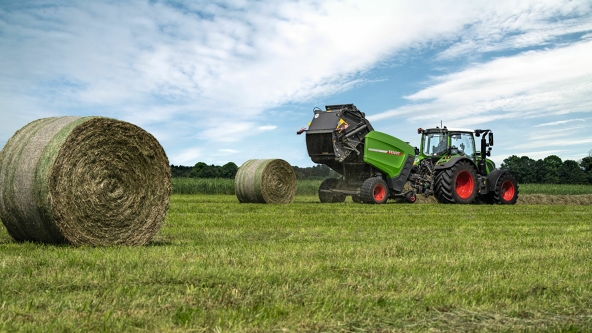 Op een veld aan de horizon rijdt een Fendt-tractor met aangekoppelde Fendt Rotana V-rondebalenpers, daarvoor twee geperste ronde balen