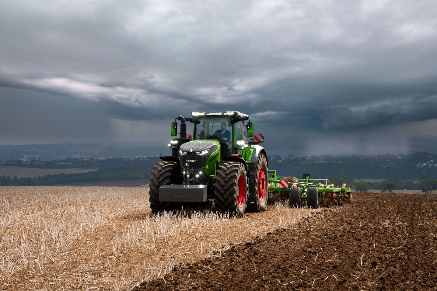 Onder een dreigende hemel met onweerswolken in de verte gaat een tractor, een Fendt 1000 Vario, onverstoorbaar verder met het werk op het veld