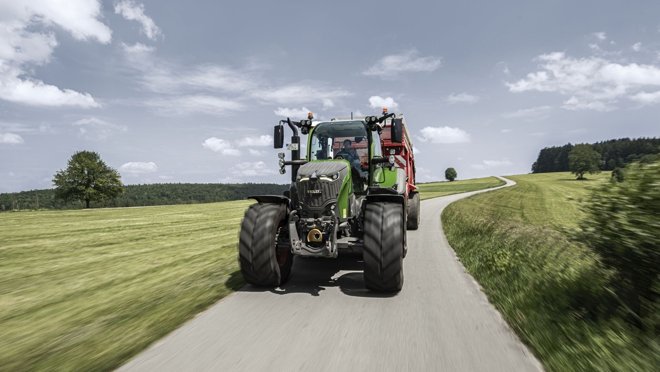 Een Fendt 700 Vario Gen7.1 met opraapwagen rijdt in de zomer over een landweg